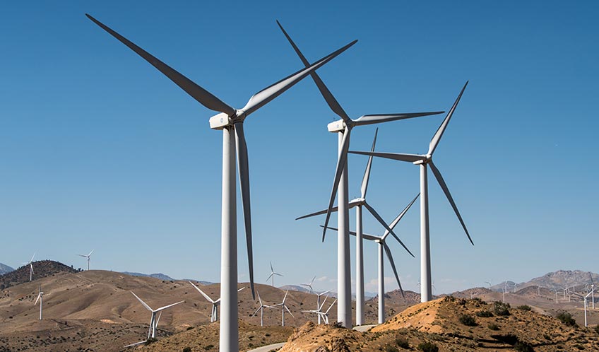 Rows of wind turbines on hilly terrain at a wind power plant.