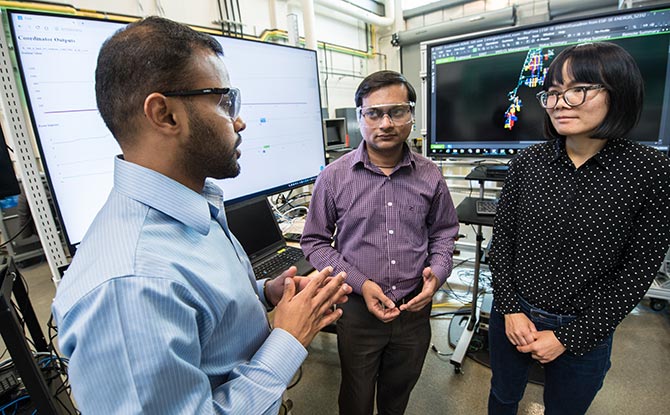 Three NREL researchers talk in front of video screen.