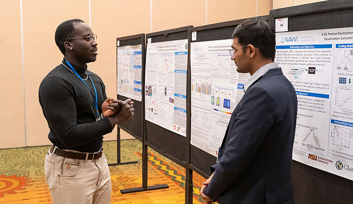 Two people discuss research poster inside hotel ballroom