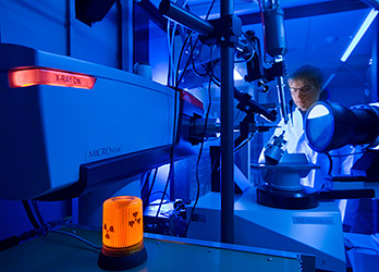 Photo of a researcher in a blue-lit laboratory using an x-ray crystallography instrument to image crystal diffraction patterns of protein for 3-D imaging of enzymes.