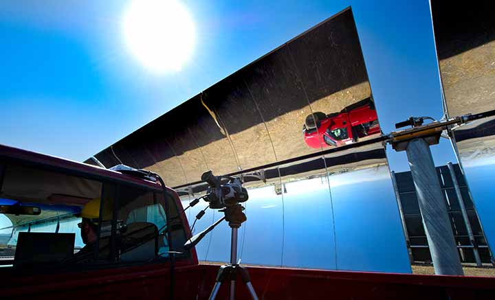 A red truck is reflected upside-down in a parabolic trough on a sunny clear day.