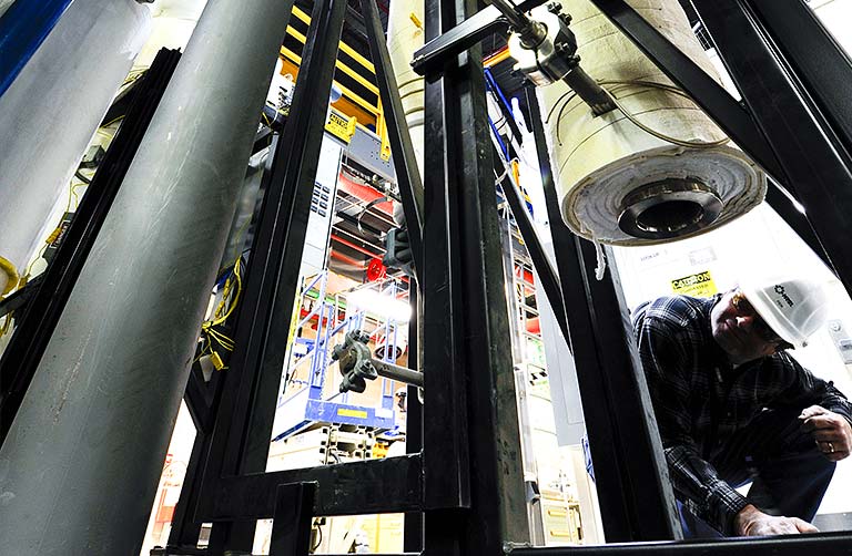 Photo of a man kneeling and looking underneath large testing equipment in an NREL facility.