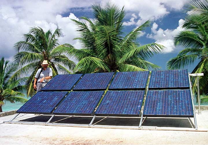 A solar photovoltaic module with palm trees and the ocean in the background.