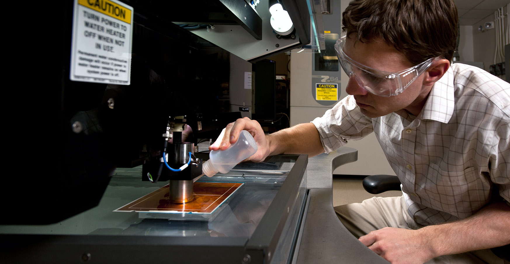 Researcher applying a liquid on a plate below lab equipment.