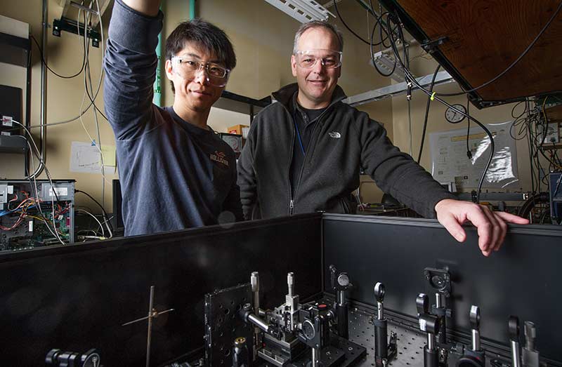 Two men stand behind a spectrometer at an NREL lab.
