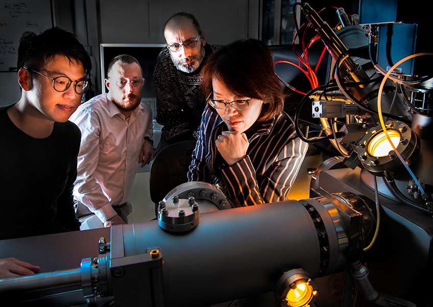 Three men and a woman look at machinery in a lab.