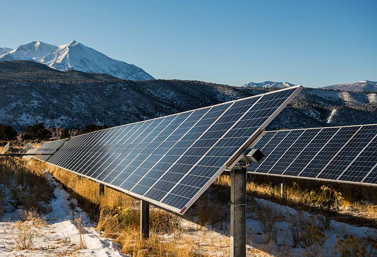 An array of solar panels in front of a snow capped mountain.