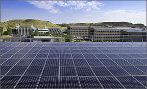 Photo of solar panels in the foreground with the NREL campus in the background, along with the grassy mesas beyond.