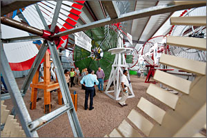 This photo shows several people assembled in a barn with the brightly colored blades of vintage windmills surrounding them. 