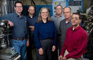 In this photo, five men and one woman stand among several large pieces of laboratory equipment.