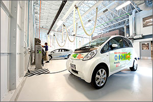 An engineer reads data from a piece of equipment mounted on the wall in a research garage. In the foreground, an electric vehicle is connected to the equipment for study. Another electric vehicle is connected behind him.