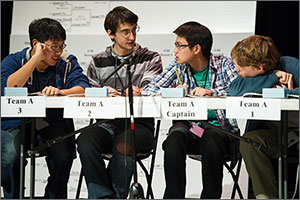 Four teenage boys sit behind a table during the 2013 Colorado High School Science Bowl, discussing the answer to a question in the final round of the competition.