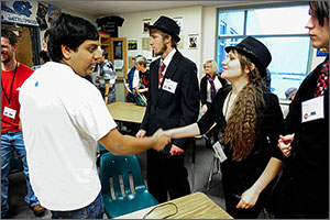 A member of one high school team shakes hands with a member of an opposing team. Several other student participants look on.