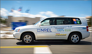 A hydrogen fuel cell powered Toyota sport utility vehicle emblazoned with an NREL logo drives past a building on the NREL campus.