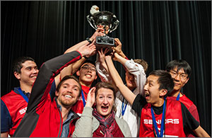 Photo of a team of high school students holding a trophy high over their coach's head.