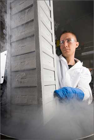 Photo of a scientist in a white lab coat in front of a tall stack of white boxes.