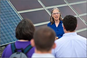 Photo of NREL's Sarah Kurtz speaking to a gathering of people with solar modules in the background.