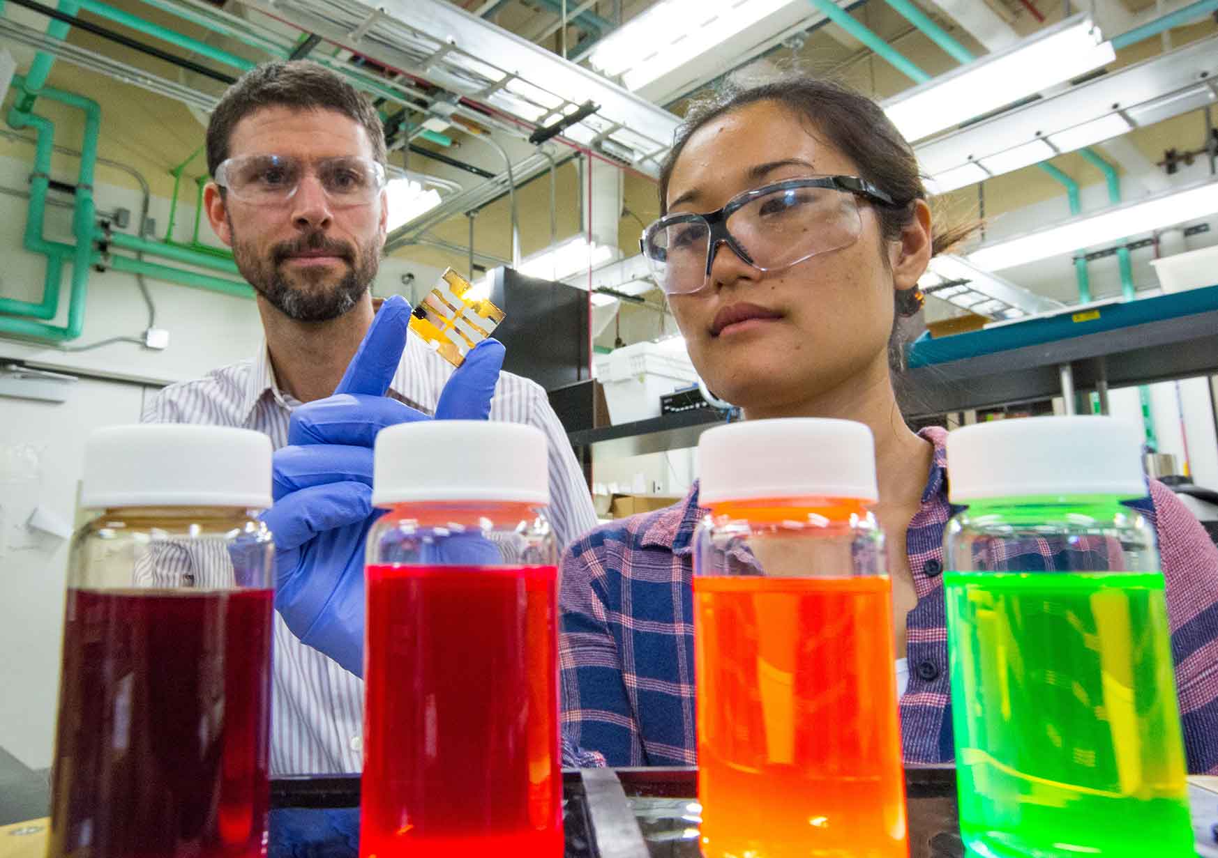 A woman holds a small thin film while a man looks on. (Photo by Werner Slocum / NREL)