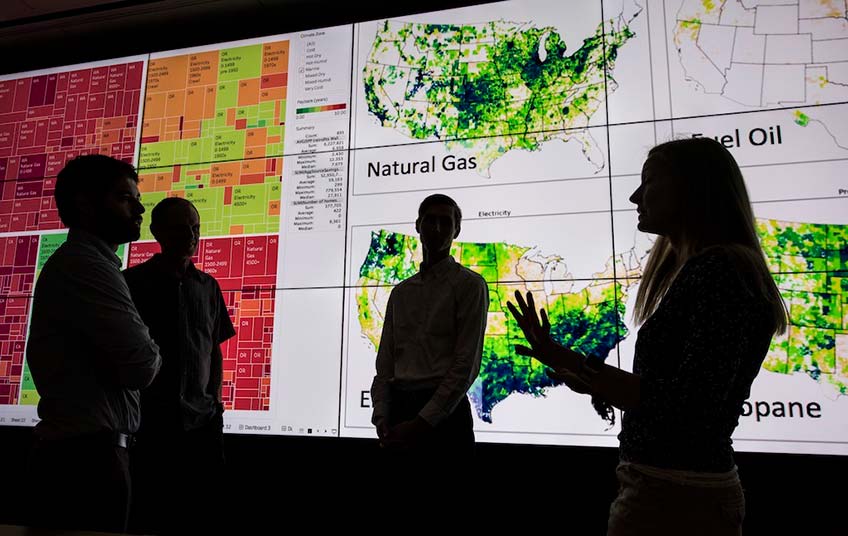 Four NREL researchers working on the ResStock building analysis tool discuss their work in front of a large visualization screen.