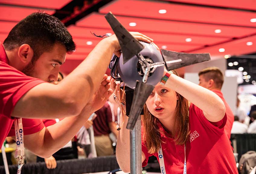 A young man (left) and young woman (right) make adjustments to their model wind turbine during the Collegiate Wind Competition. 