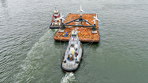 A boat pushes a barge carrying underwater turbine blades