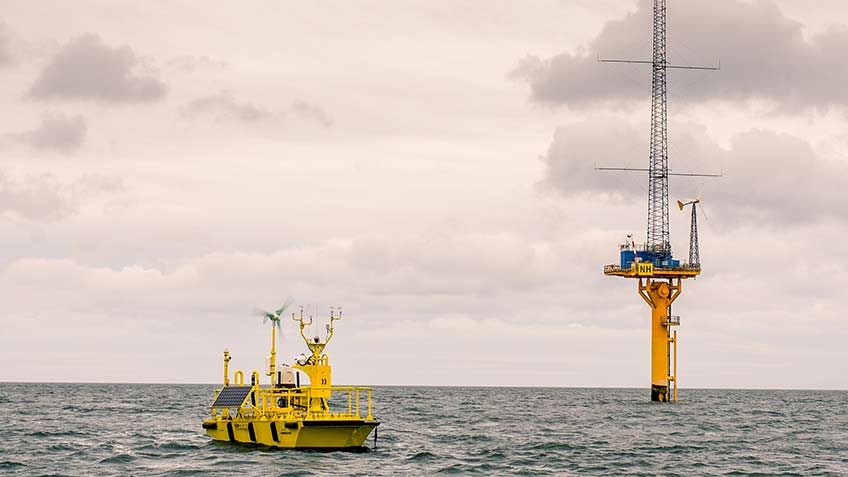 Photo of a floating lidar buoy in the ocean, and next to a meteorological tower.
