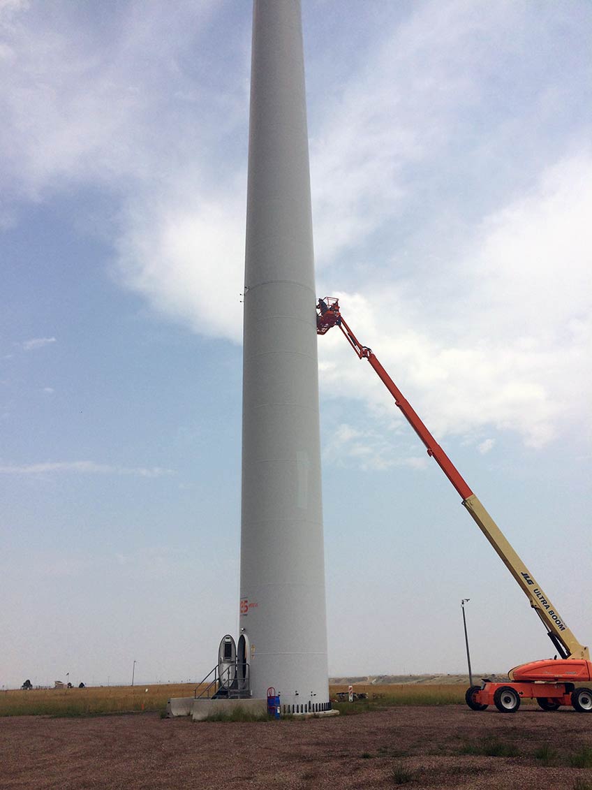 A crane with a man atop it installs UV lights on a wind turbine tower. 