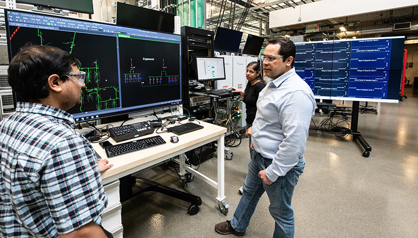NREL researchers collaborate in the lab, surrounded by large computer screens.