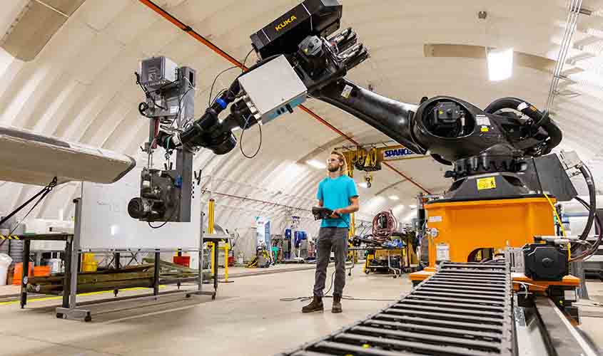 An intern uses a remote to move a robotic arm over a wind turbine blade in a research facility