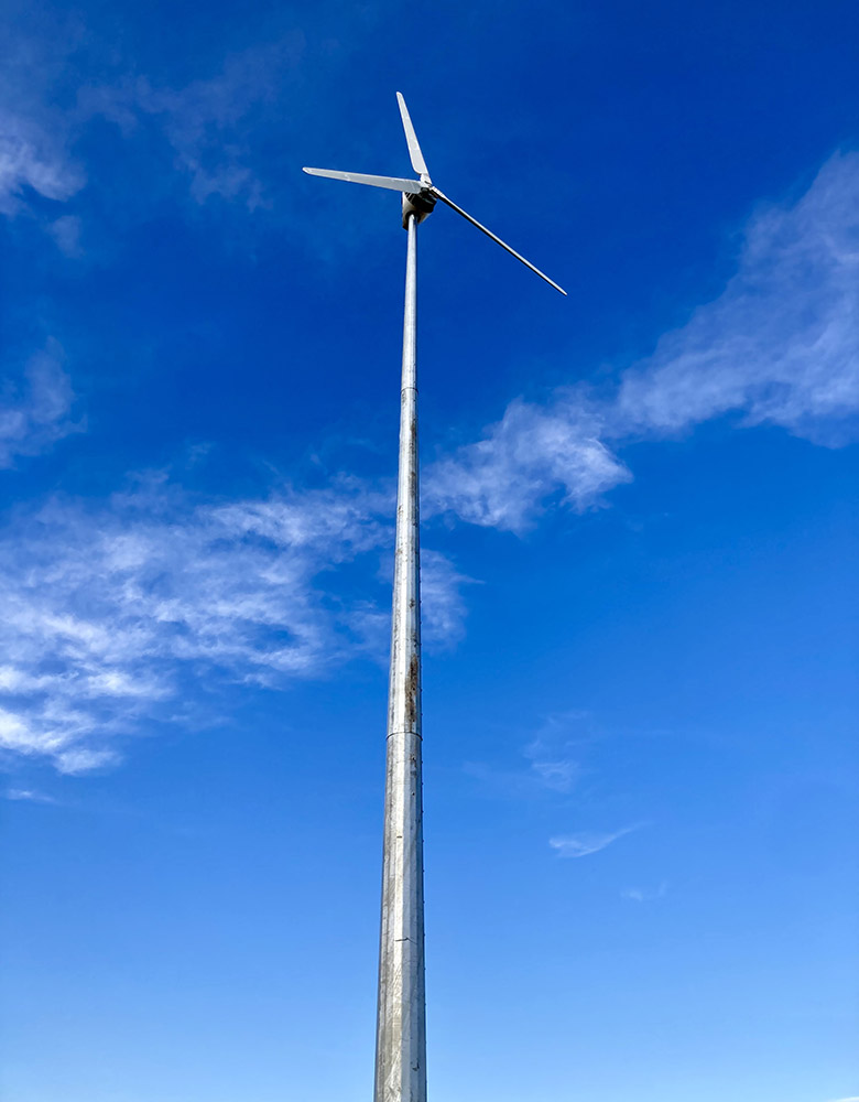 A wind turbine in a grassy field with people, vehicles, and equipment at its base.