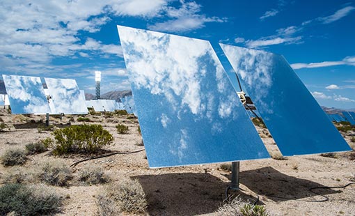 Picture of heliostats in a desert with blue sky and sunlight reflecting off them.