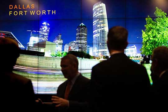 Photo of four people standing near an image of the Dallas-Fort Worth skyline.