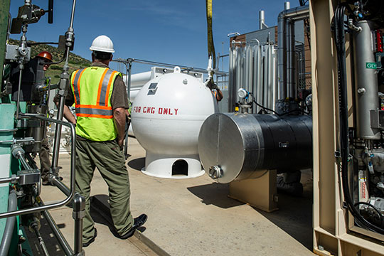 Two men in hard hats supervise installation of a natural gas storage tank.