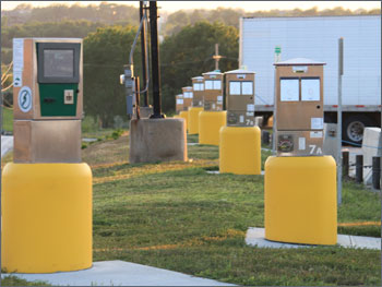 Photo of series of truck stop electrification pedestals near highway with heavy-duty truck parked in the background.