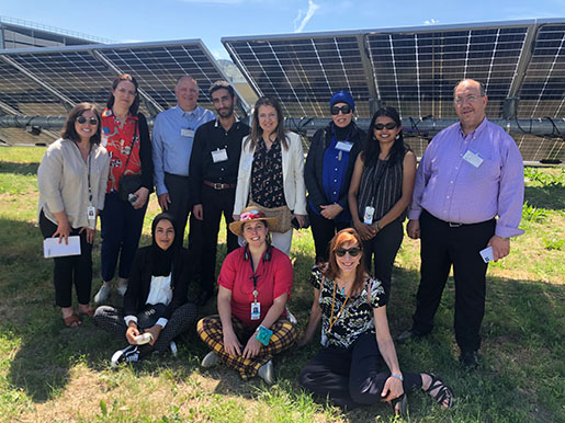 A group of people standing and sitting next to solar panels.