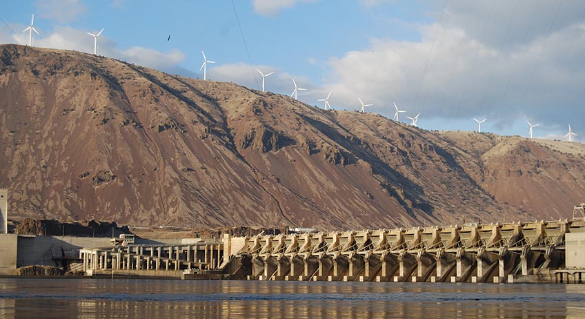 Photo of wind turbines on a hill above a hydropower dam.