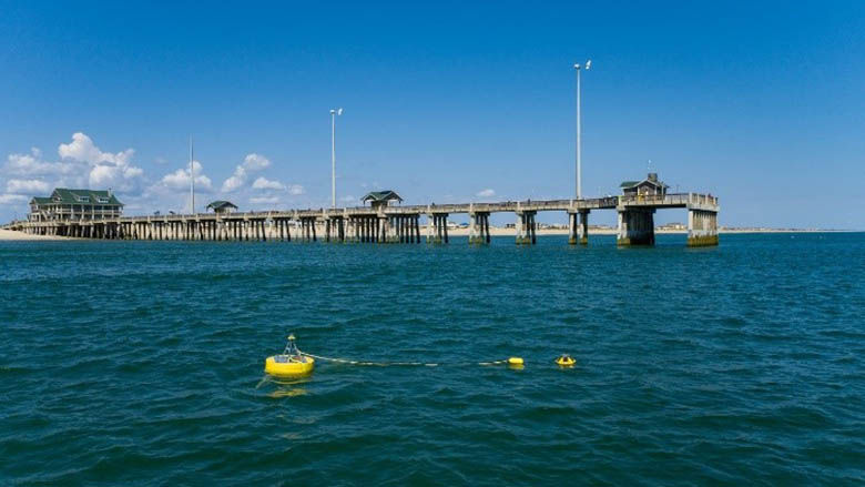 Yellow buoy floats in the ocean in front of a pier