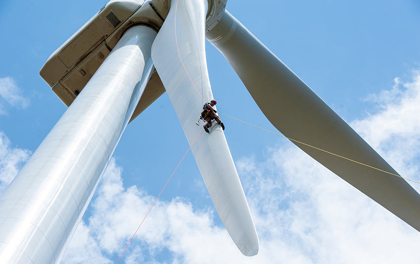 A person scales one of a wind turbine's blade in a harness.