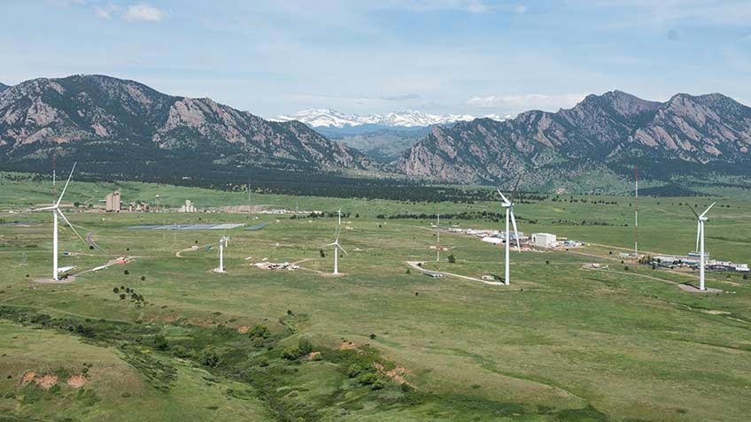 A field of wind turbines with mountains in the background.