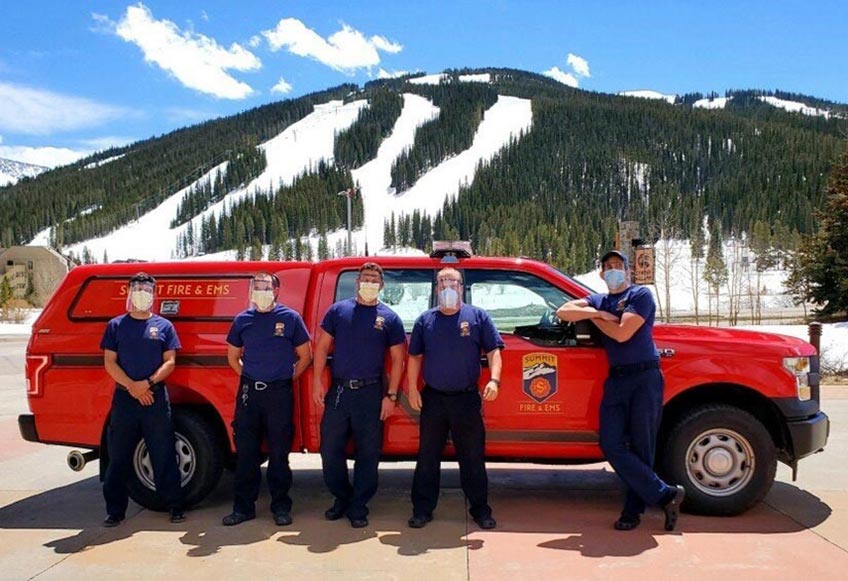 Firefighters stand in front of an emergency vehicle