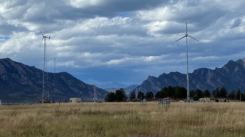 Two small wind turbines in front of a mountain range.