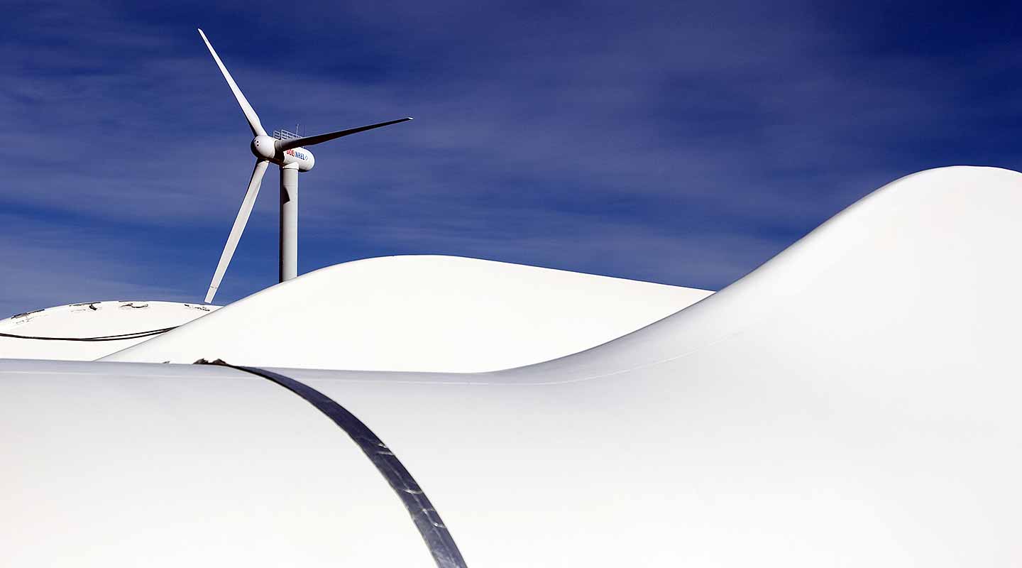 A photo of a wind turbine against blue sky with white blades on their sides in the foreground.