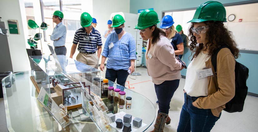 A group of people in hard hats view specimens in bottles and an architectural rendering on a table.