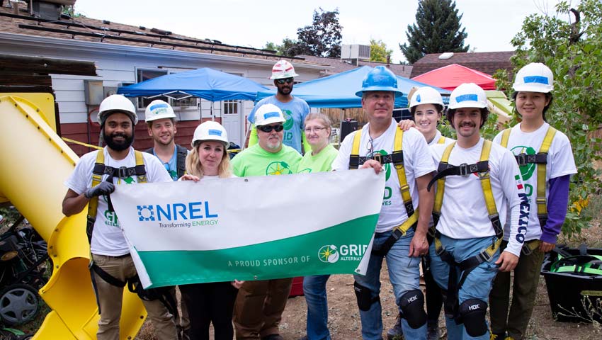 10 people in hard hats standing in front of a house holding a banner bearing "NREL - Transforming Energy: A proud sponsor of Grid Alternatives."