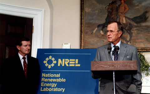 A person speaking at a podium as another looks on.