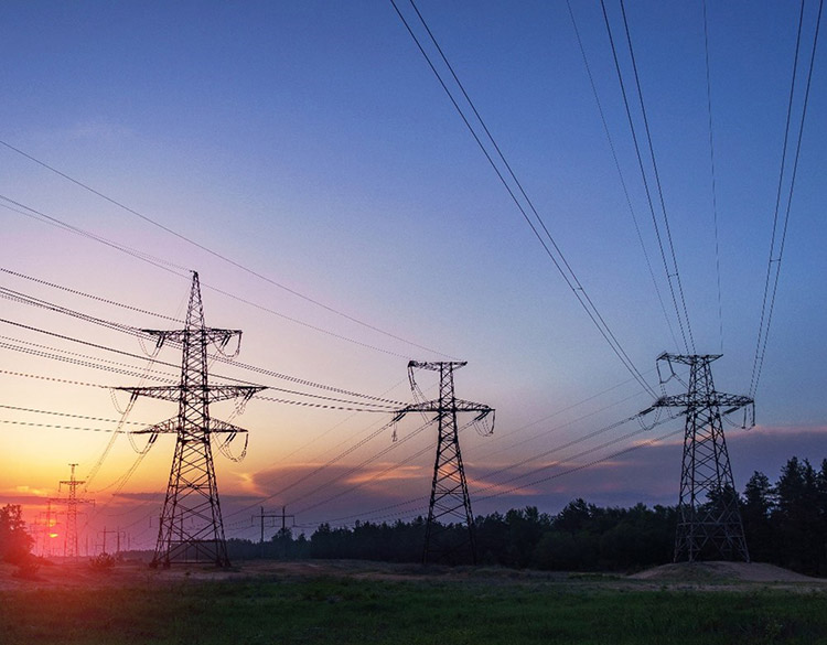 Transmission towers in a rural setting with a sunset in the background.