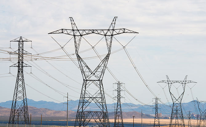 Photo of transmission towers with a solar field and mountains in the background.