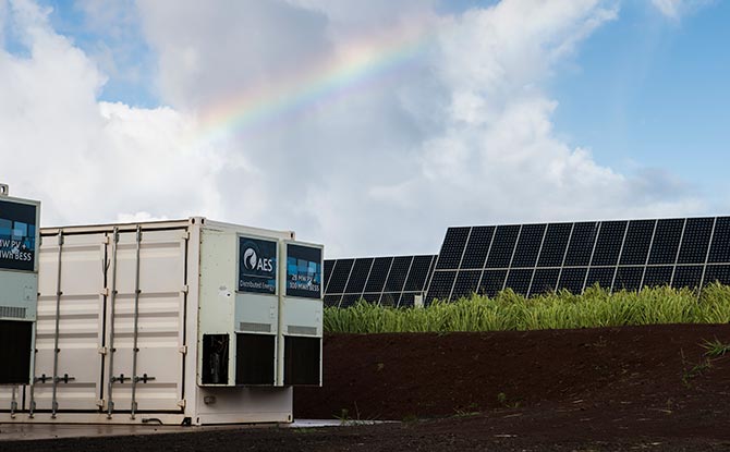 Photo of energy storage with solar panels in the background, showing that storage and solar tend to go well together operationally.