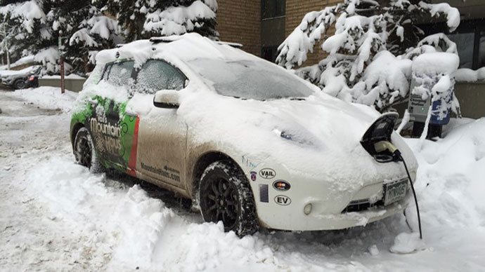 Photo of a charging electric vehicle covered in snow surrounded by a winter backdrop.