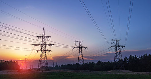 Transmission towers in a rural setting with a sunset in the background